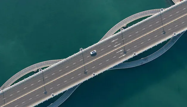 Overhead view of a multilane road bridge crossing blue-green water