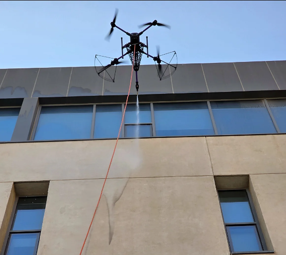 Hose-connected cleaning drone beside a building façade and windows