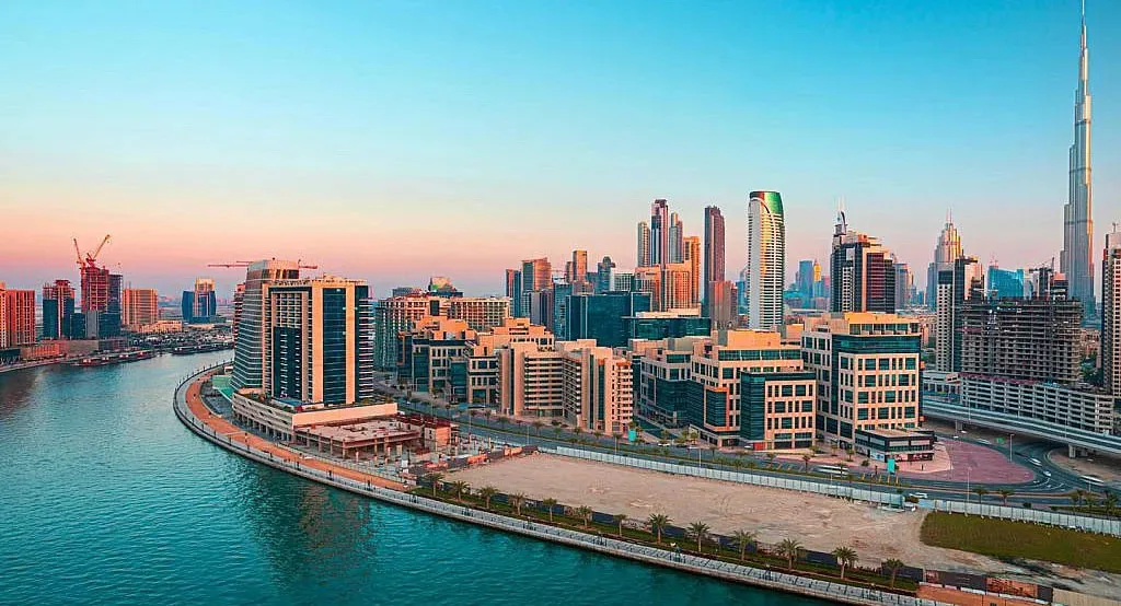 An elevated waterfront view shows modern towers, a curved shoreline and the Burj Khalifa in the distance