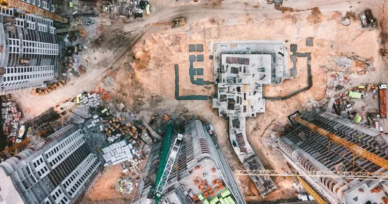 A top-down aerial photograph shows an active building site surrounded by roads and neighboring structures