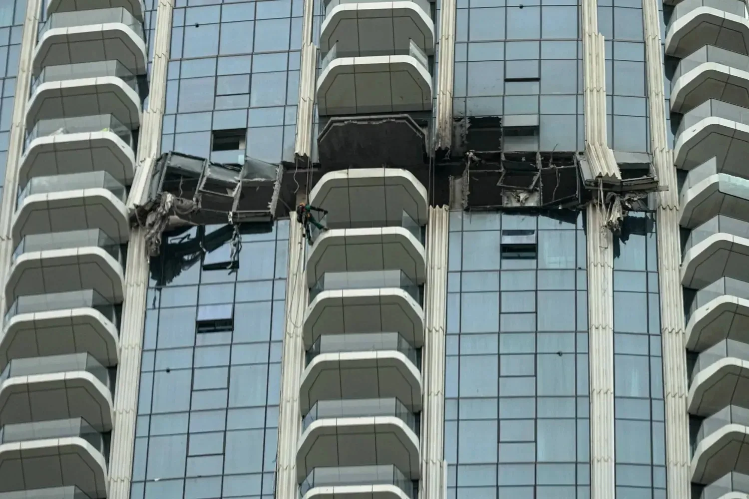 Suspended work platforms hang beside a high-rise glass facade with repeating balconies